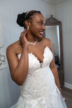 Bride wearing strapless lace wedding gown and veil poses against white wall.