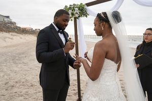 Wedding vows being exchanged under a wooden arch on a sandy beach.