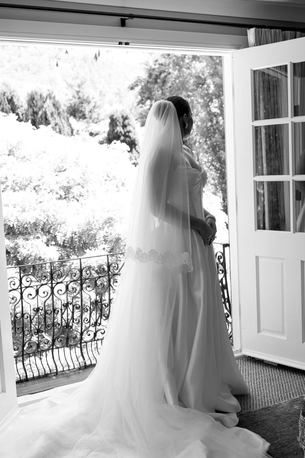 Black and white photo of a bride in a flowing gown and veil standing in an open doorway overlooking a balcony.