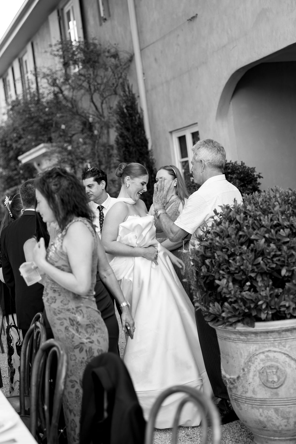 Black and white photo of a bride in white gown greeting guests at an elegant outdoor wedding reception.