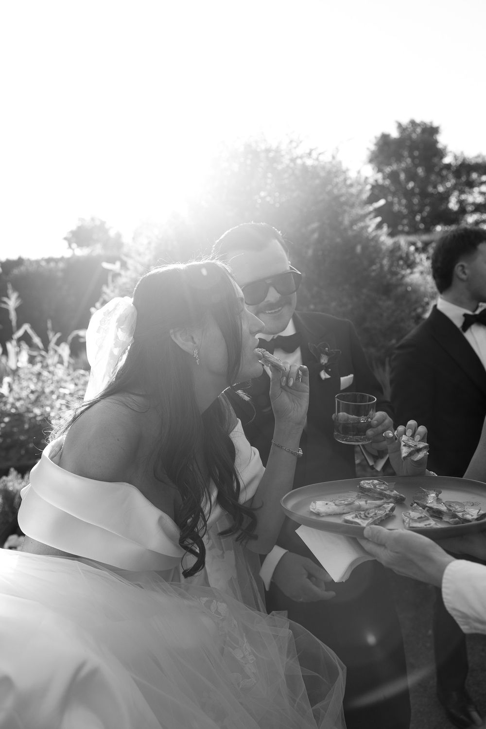 Black and white photo of a bride and groom sharing a moment outdoors at their wedding reception in bright sunlight.