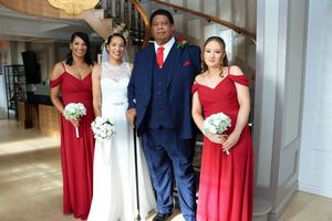 Wedding party in red and navy attire poses together in an elegant indoor venue with white columns.