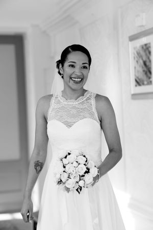 A bride in a white lace wedding dress holds a bouquet of white roses in a bright indoor setting.