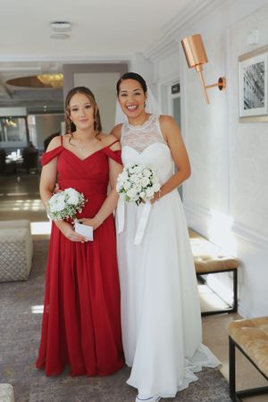 Wedding party members in red bridesmaid dresses and white bridal gown pose together in an elegant indoor setting.