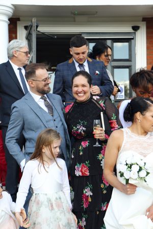 Wedding guests gather outside venue in formal attire with floral dresses and suits for celebration.