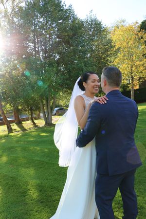 A couple shares a romantic moment outdoors in a sunlit park setting with autumn trees in the background.