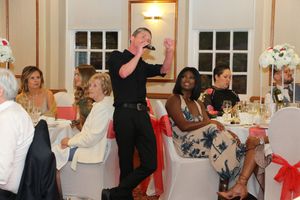 A group of people dancing together at a formal event in an elegant white-walled room with chandeliers.