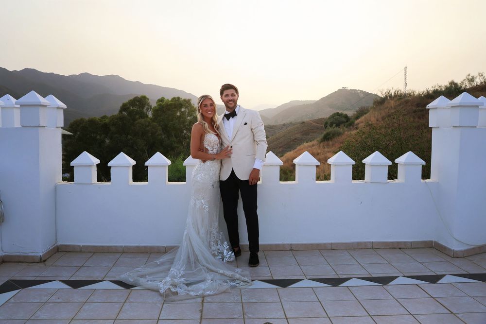 Bride and groom posing on a white terrace with mountain sunset views at their outdoor wedding ceremony.
