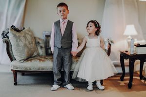 A wedding party stands together in formal attire with shoes and feet visible in a bright interior space.