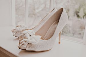 Elegant ivory satin wedding shoes with bow details arranged in a row against a light background.