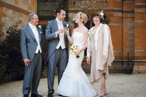 Wedding party celebrates joyfully outside a historic brick building on a sunny afternoon.