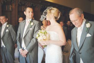 A wedding party in formal attire stands in a row wearing gray suits and holding bouquets during an elegant ceremony.