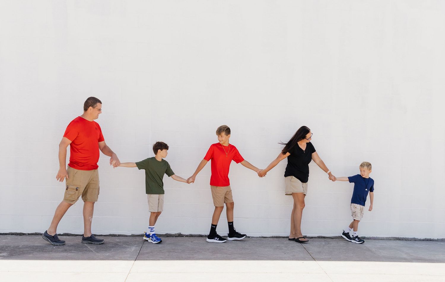 A sequence of connected people bending forward in a wave-like motion against a white wall.