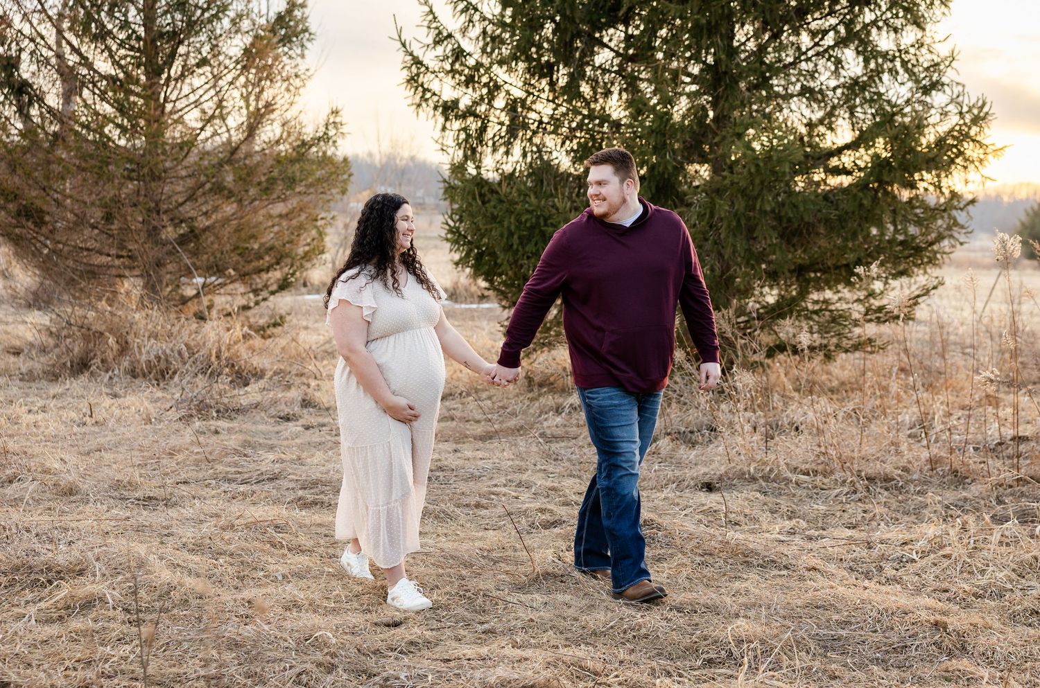Two people walk together on a scenic path during golden hour as sunlight filters through trees in the background.