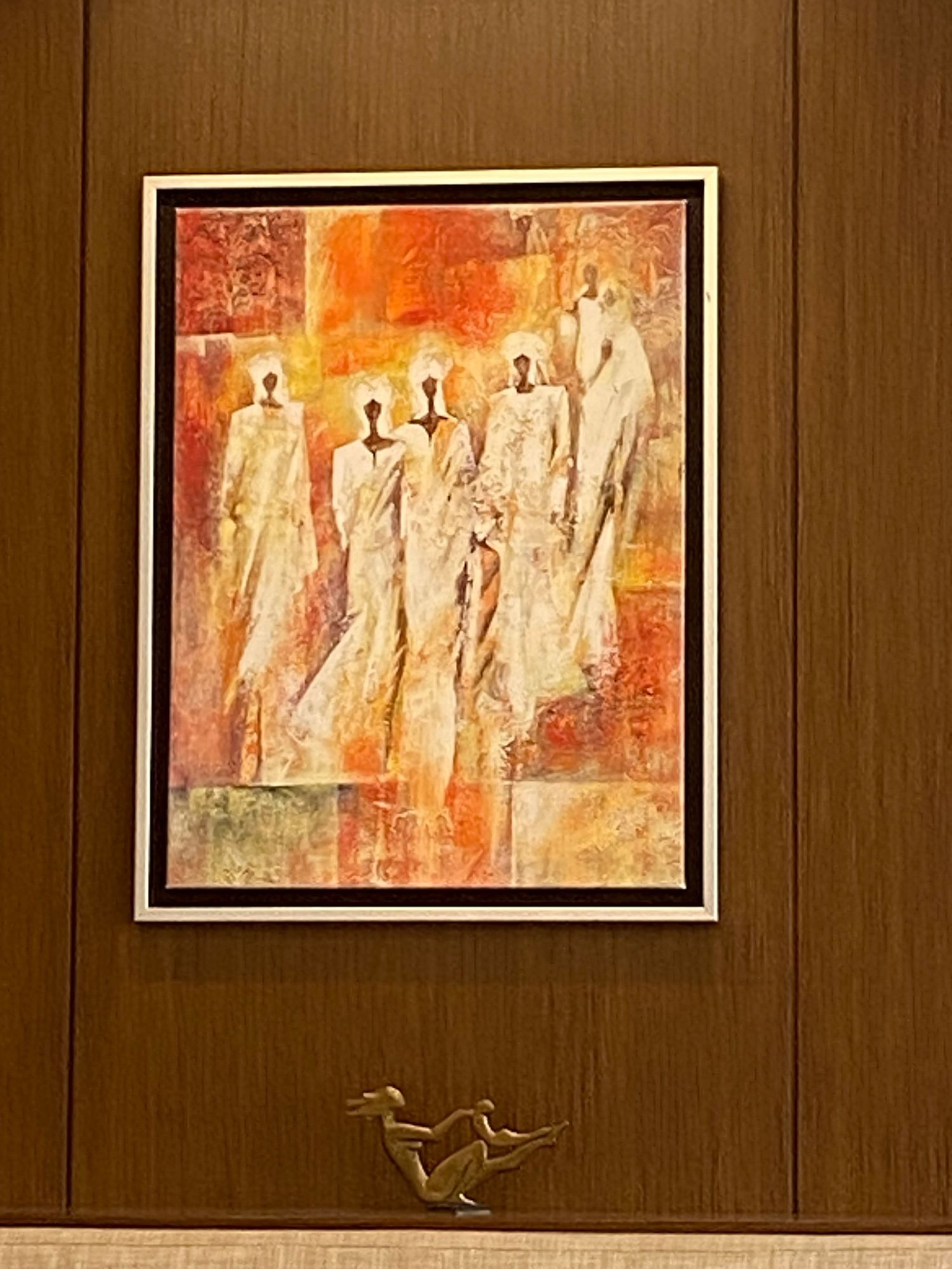 A series of abstract paintings with warm orange and red tones displayed on a wooden paneled wall.