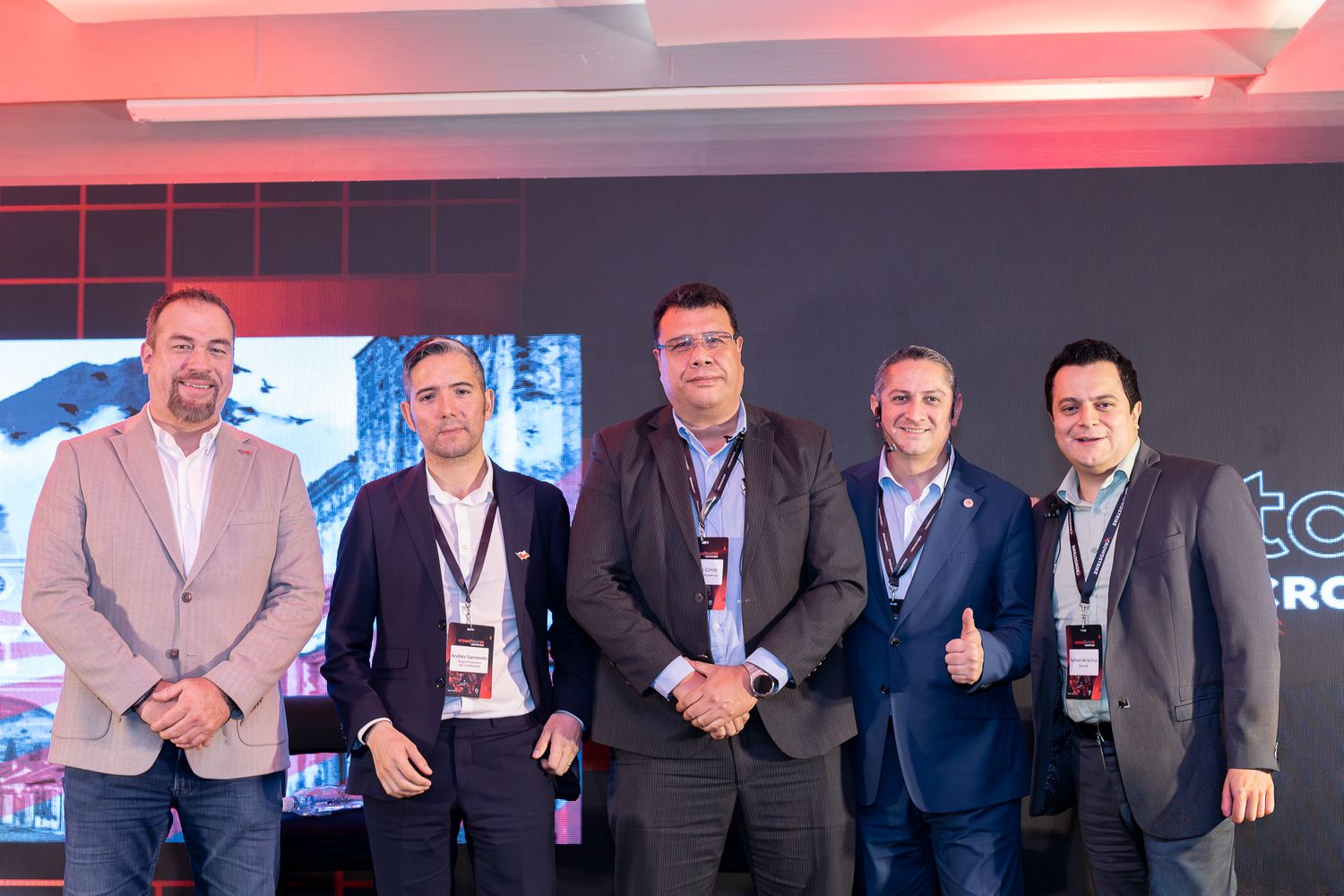 Group of business professionals standing together on stage at a technology conference with red lighting effects.