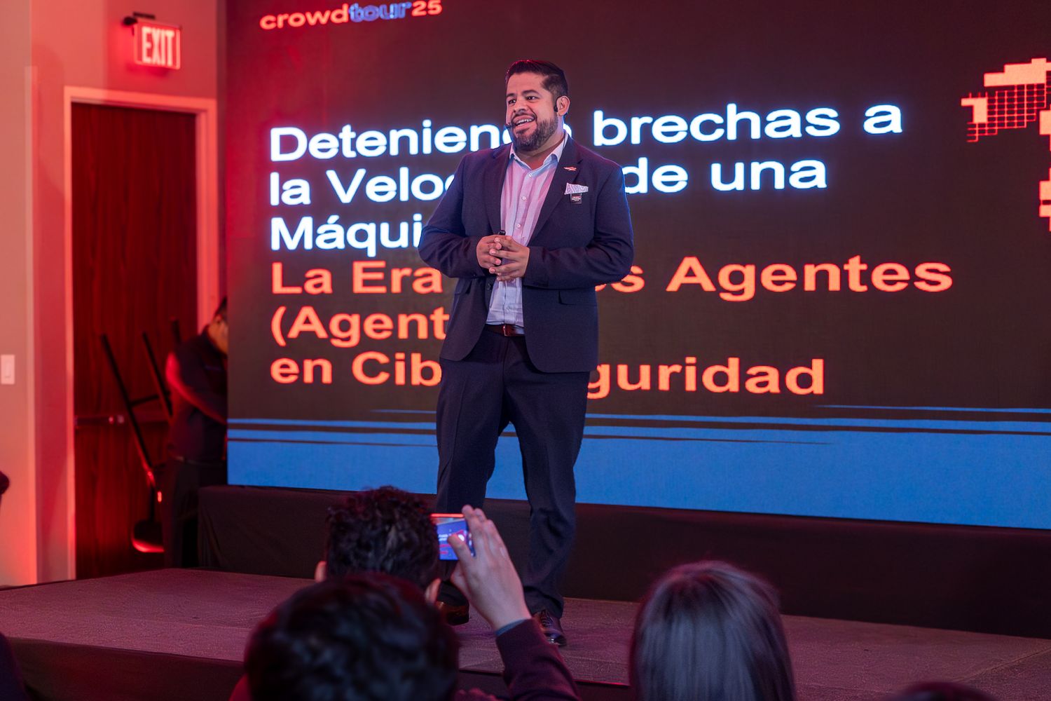 Conference presentation stage with red lighting and digital screens displaying cybersecurity related text.