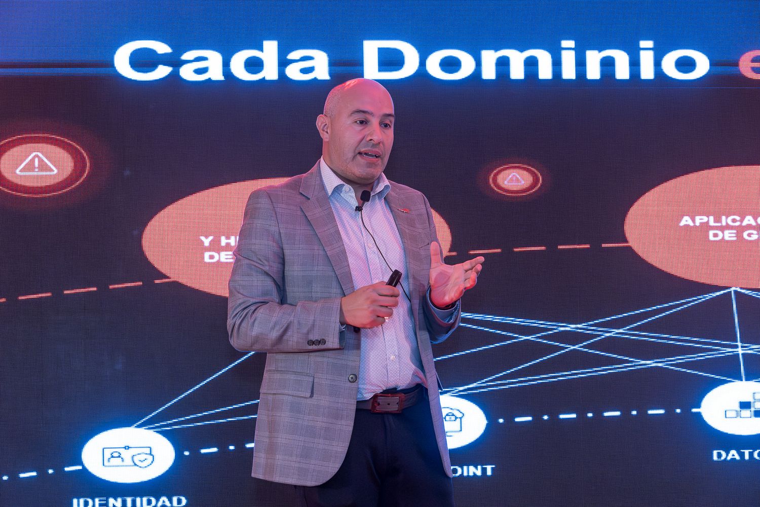 Business presentation on stage with large digital display screens showing data visualization and graphs.