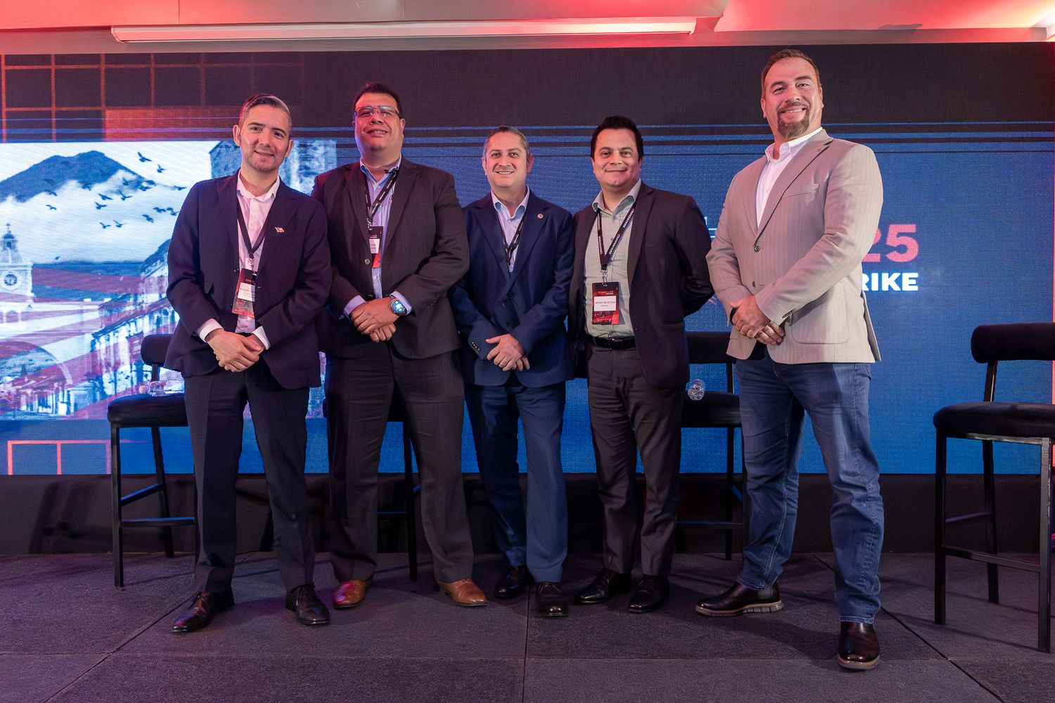 Corporate executives and team members posing together at a business conference with blue and red stage lighting.