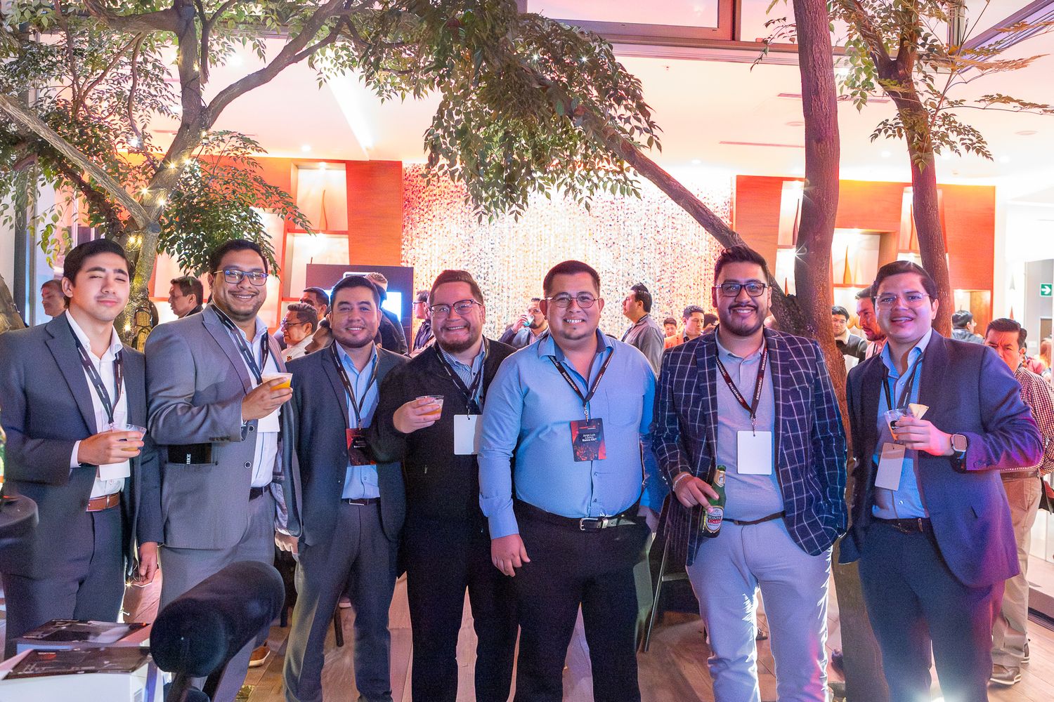 A group of professionally dressed people gather outdoors at a networking event with drinks in hand.
