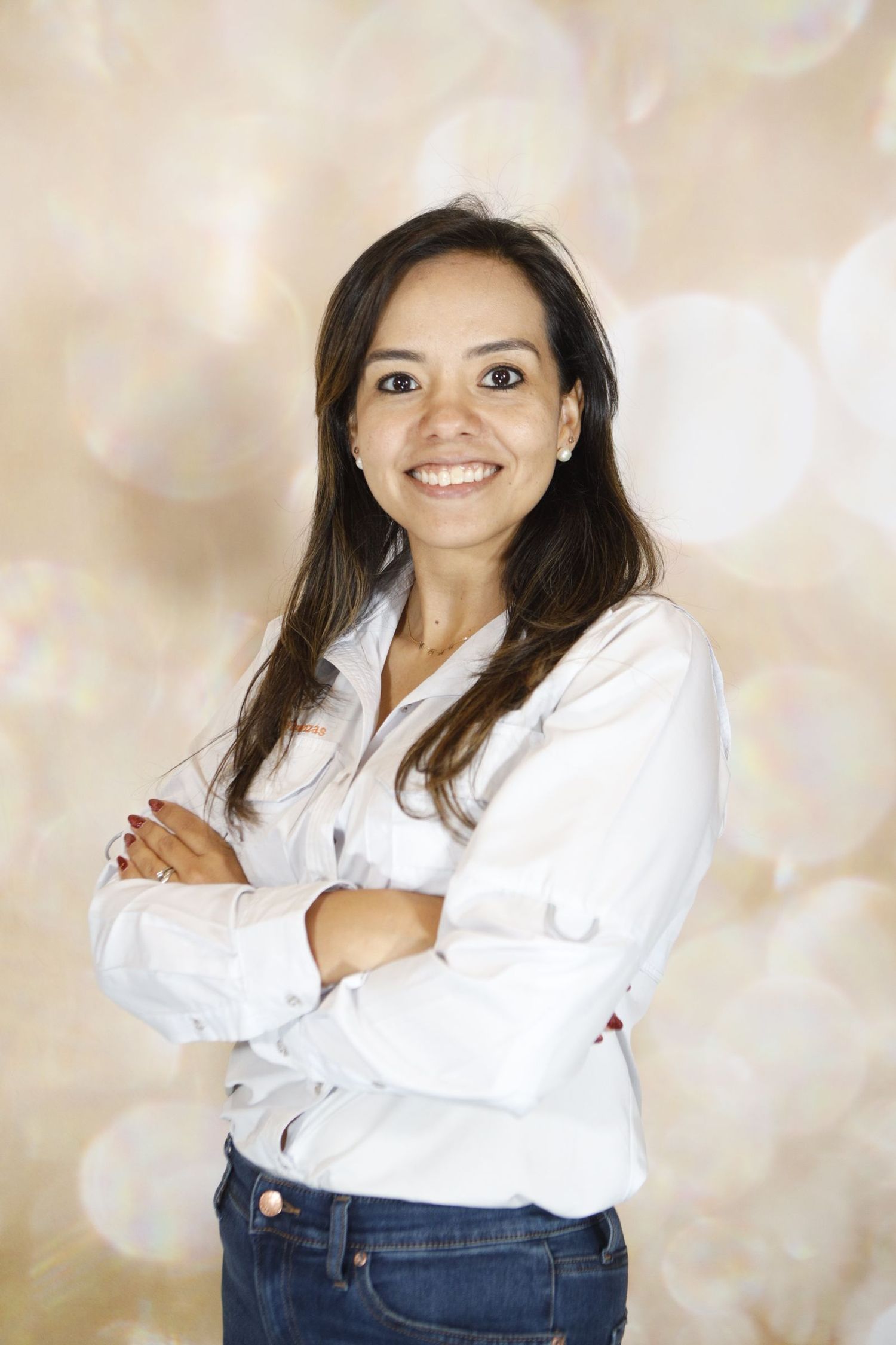 Professional portrait of woman in white button-up shirt and jeans against light bokeh background.