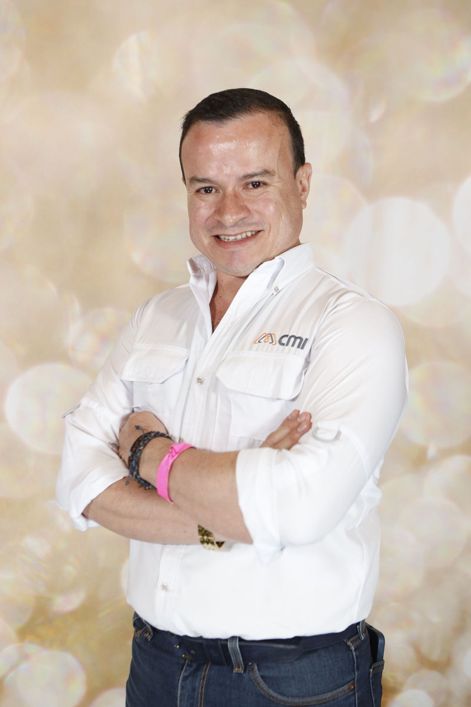 Professional headshot of someone in a white dress shirt with crossed arms against a light beige background.