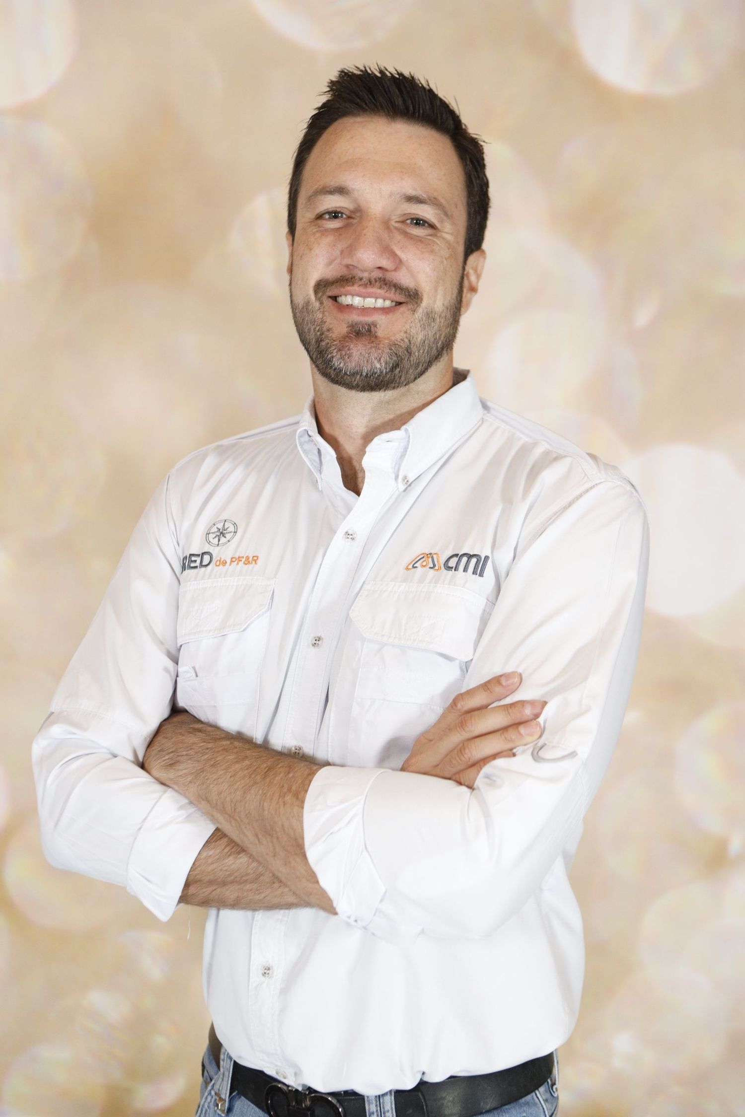 Professional in white chef coat standing confidently with arms crossed against light bokeh background.