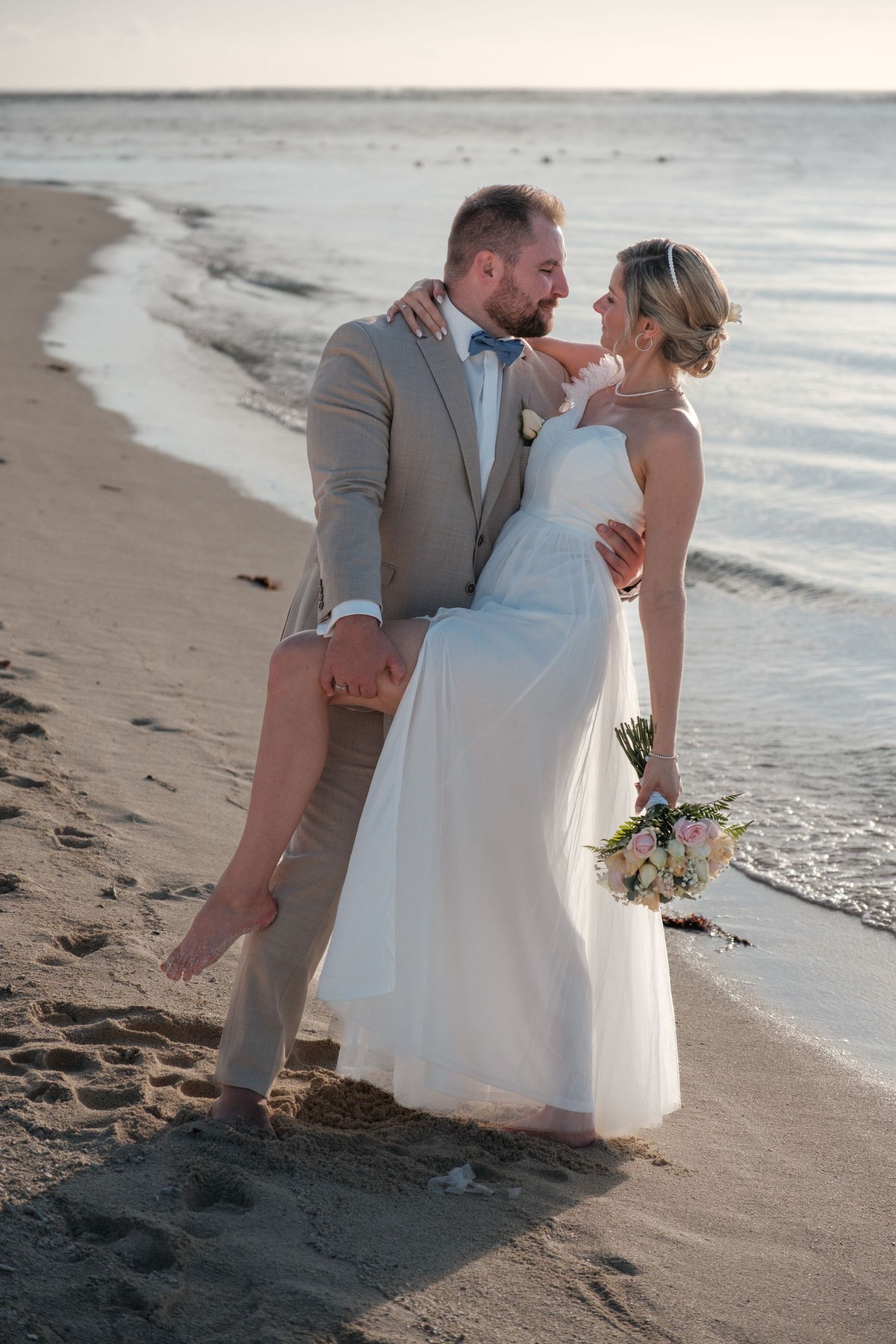 Couple shares romantic moments on sandy beach at sunset with gentle waves in background.