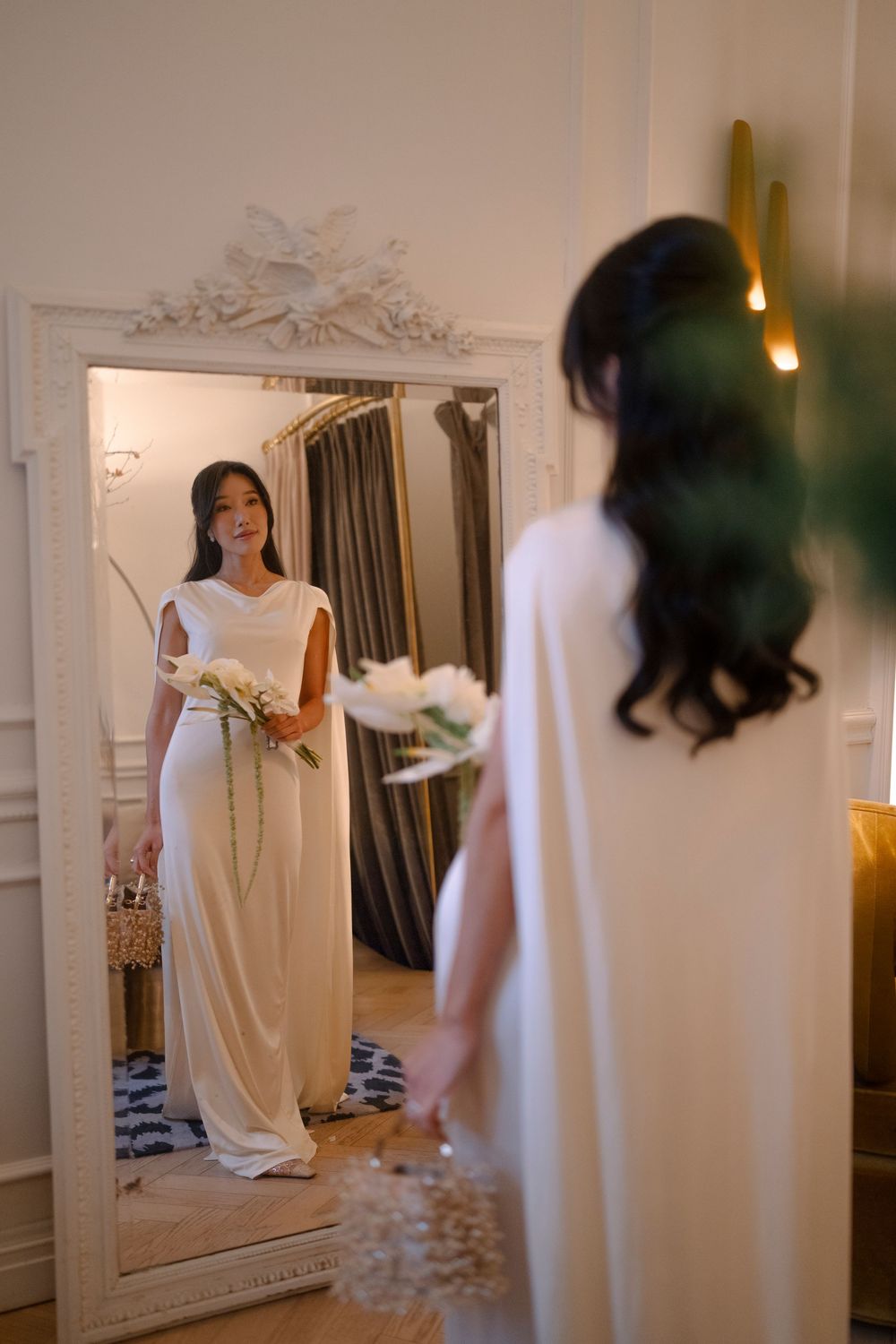 A series of mirror reflections show a person in a flowing white dress preparing in an elegant room with warm lighting.