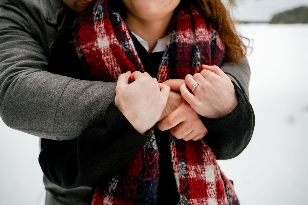 Close up of hands crossed over chest wearing a cozy gray sweater and red plaid scarf in winter.
