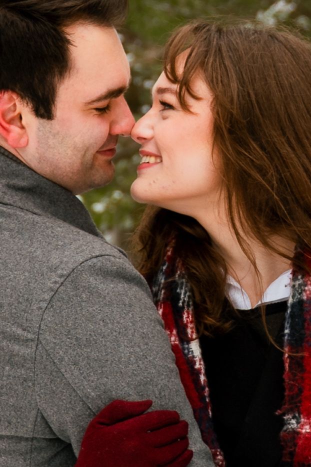 A romantic couple in winter attire share an intimate moment outdoors with snowy scenery in the background.