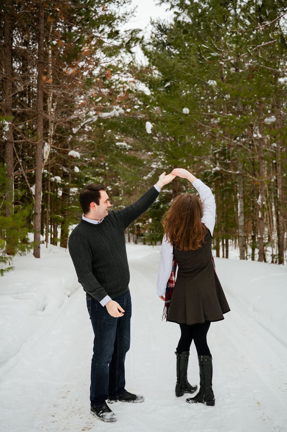 Playful couple throws snow at each other on a tree-lined winter path.