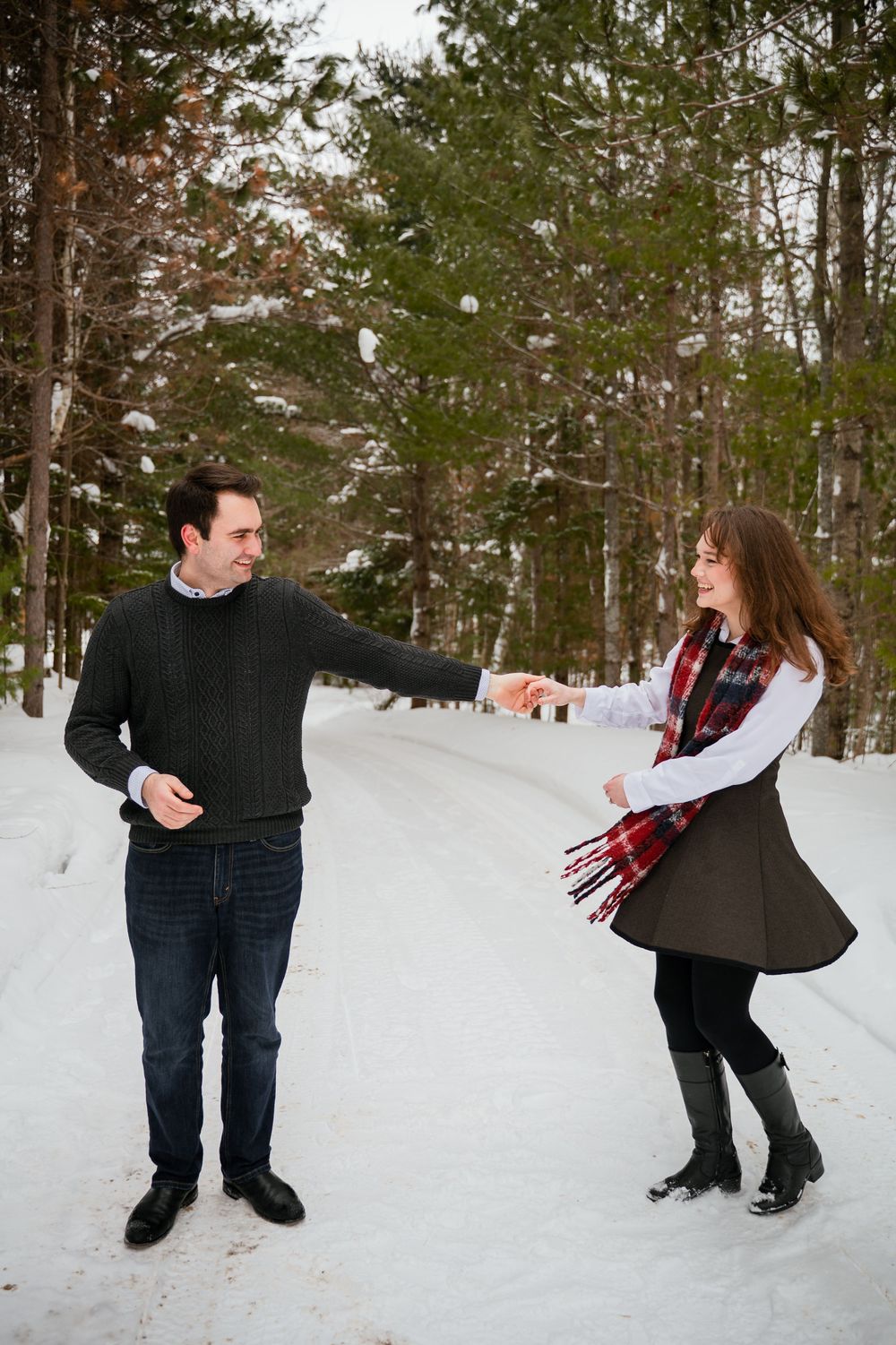 A playful couple dances together in a snowy winter forest setting.