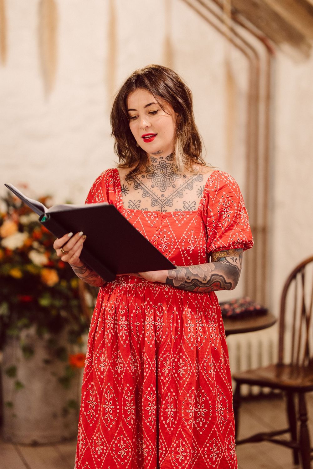 A person in a vibrant red patterned dress sits looking at a menu in an elegant restaurant setting.