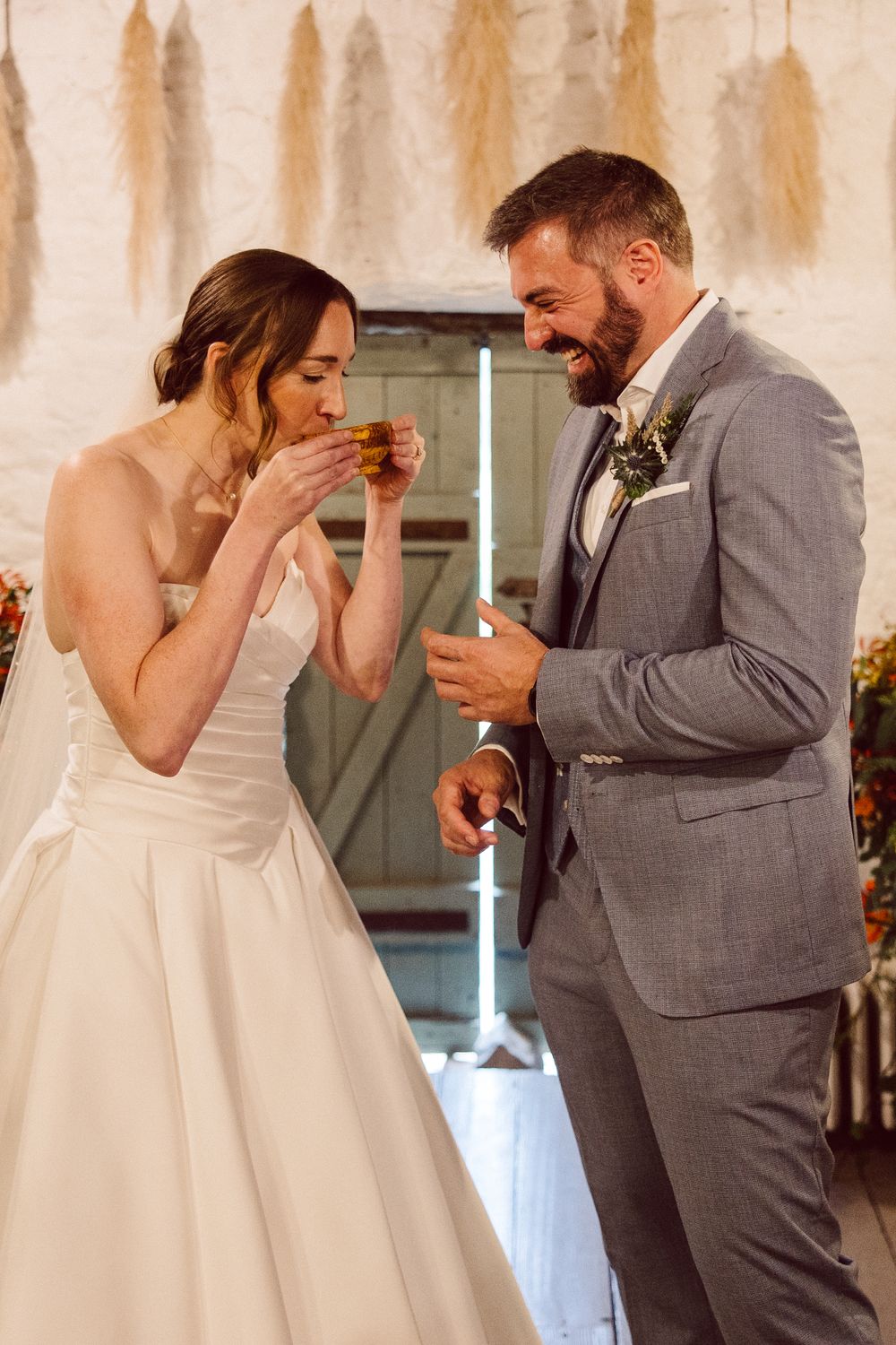 A bride and groom in formal wedding attire share a playful moment eating tacos during their reception celebration.
