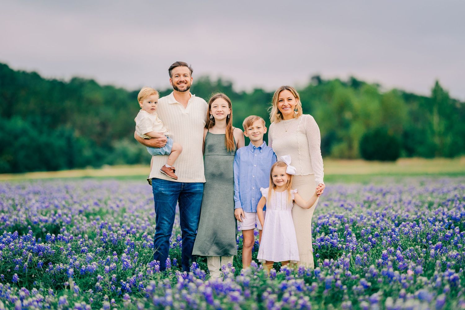 Family posing together in bluebonnet field for a spring mini session in Central Texas with vibrant wildflower backdrop.