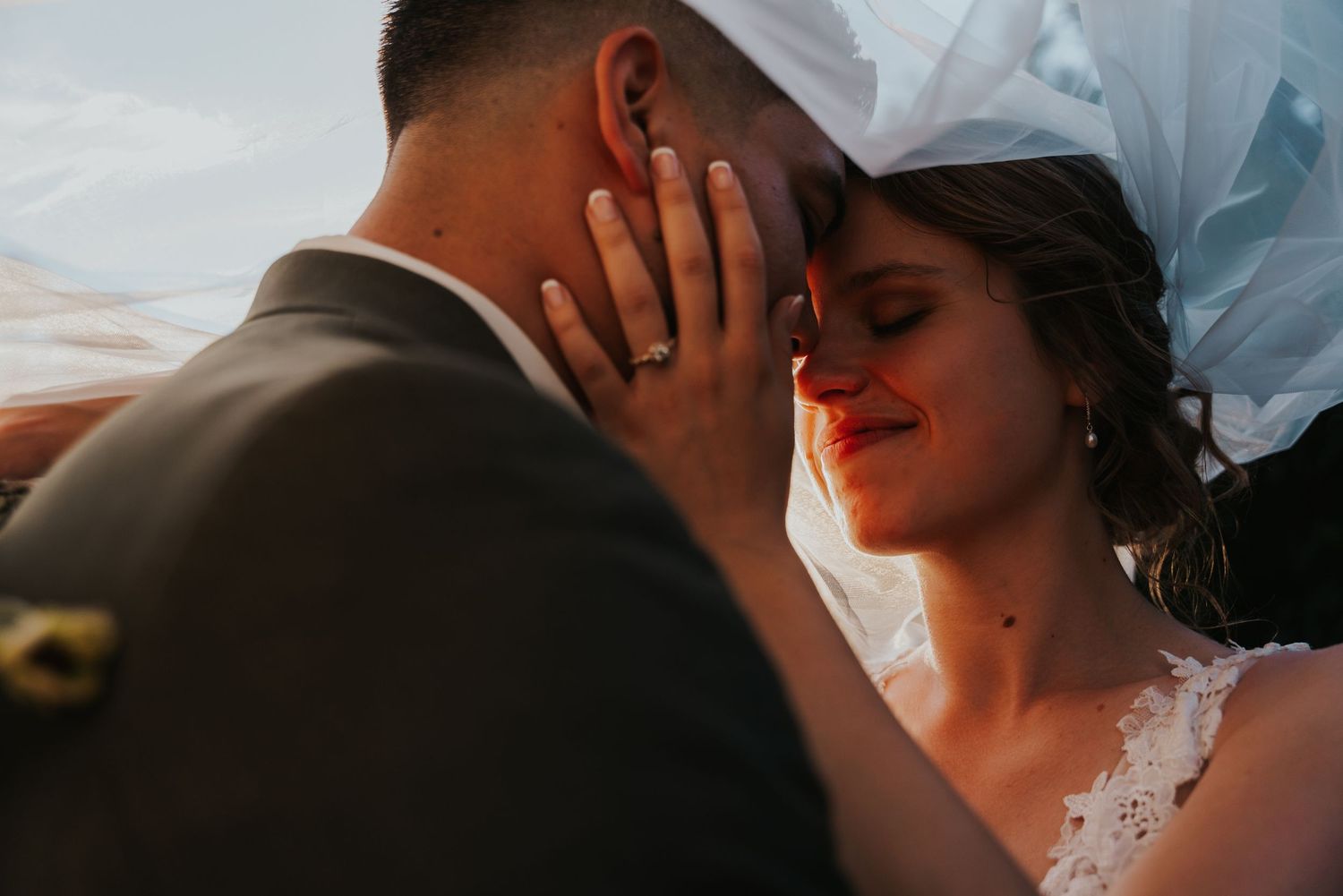 Wedding couple shares romantic kisses in a garden setting with vibrant floral arrangements and white drapery.