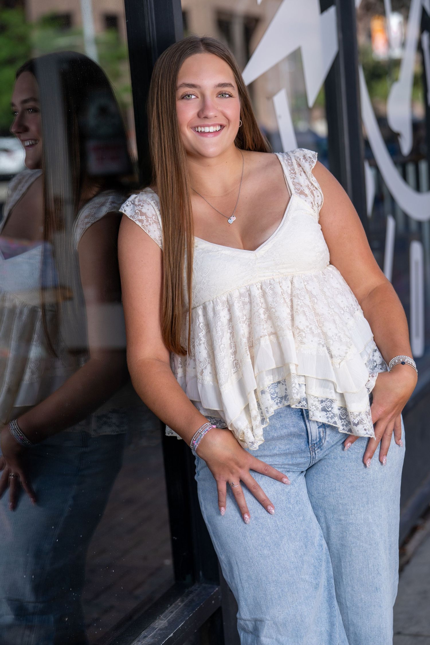 A person in a white lace top and light blue jeans poses casually against a dark background.