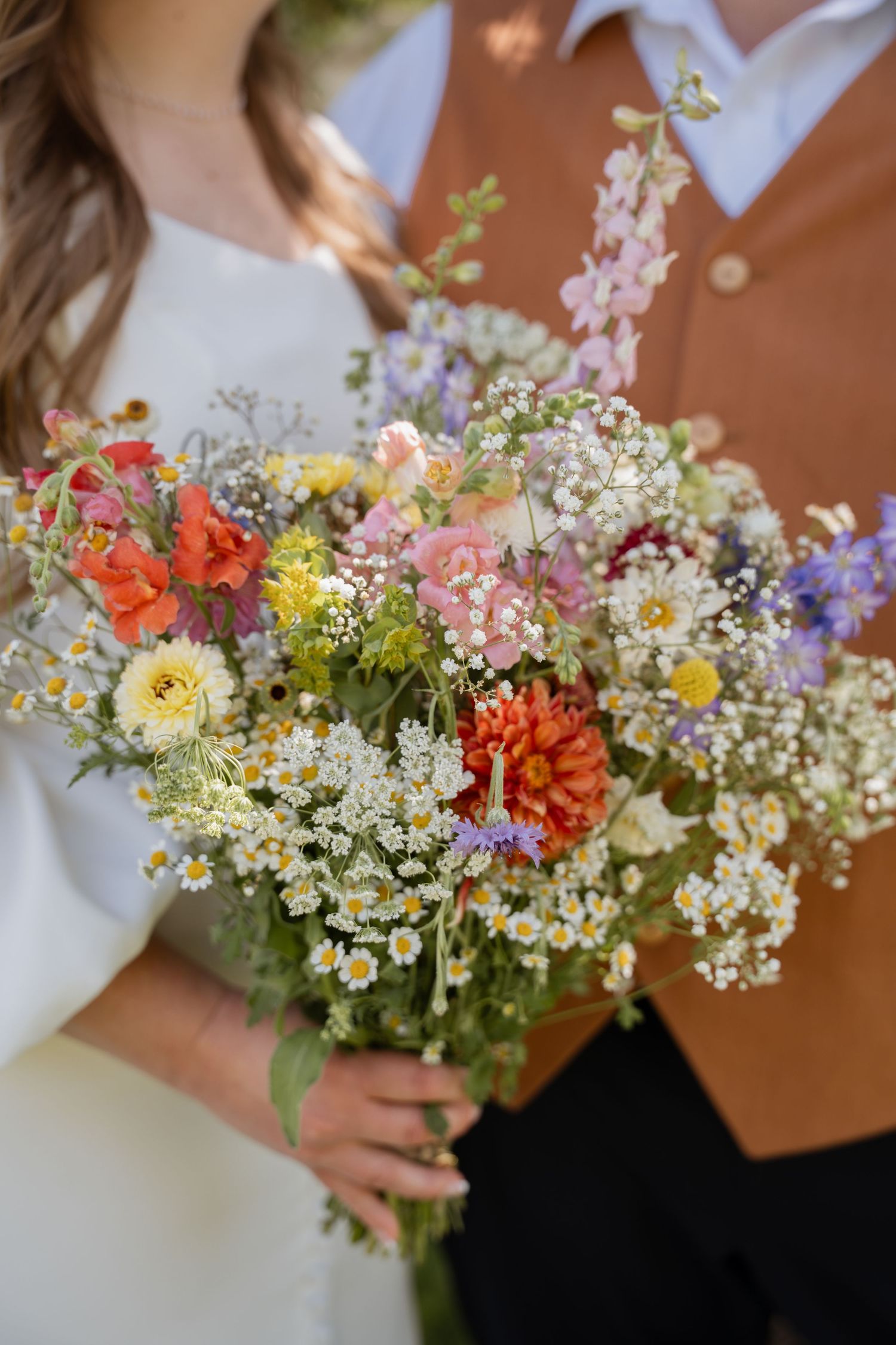 Bride and groom embracing beneath a tree with a detail shot of the bride's wildflower bouquet in Des Moines, Iowa.