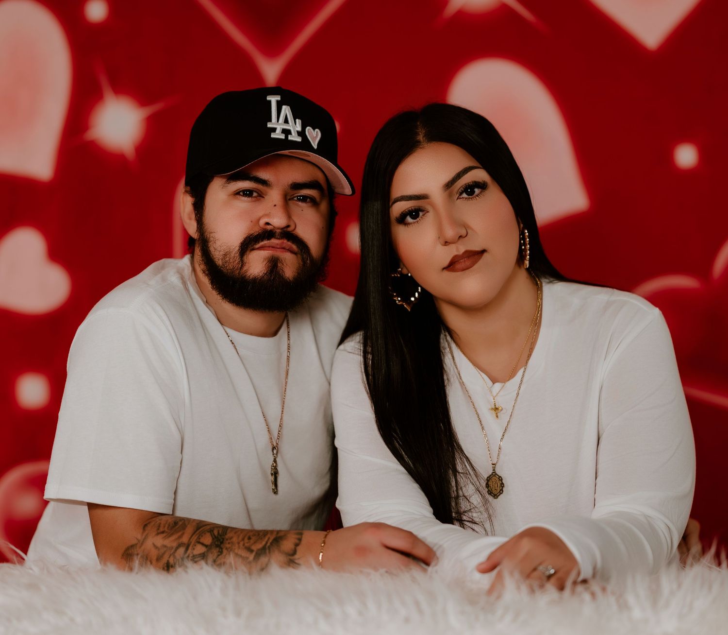 Couple posing for romantic Valentine's Day themed photo shoot with red heart decorations in the background.