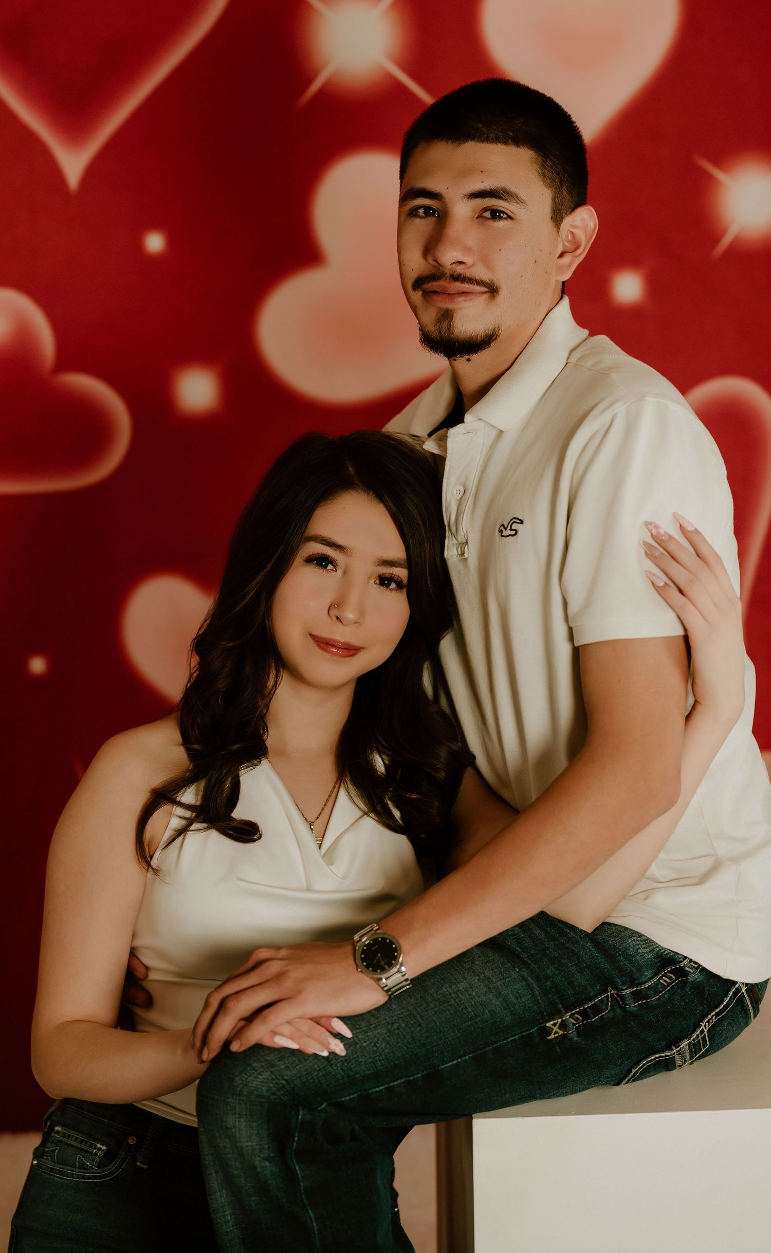 Romantic couple photoshoot with red heart bokeh backdrop showing intimate poses in white and black attire.