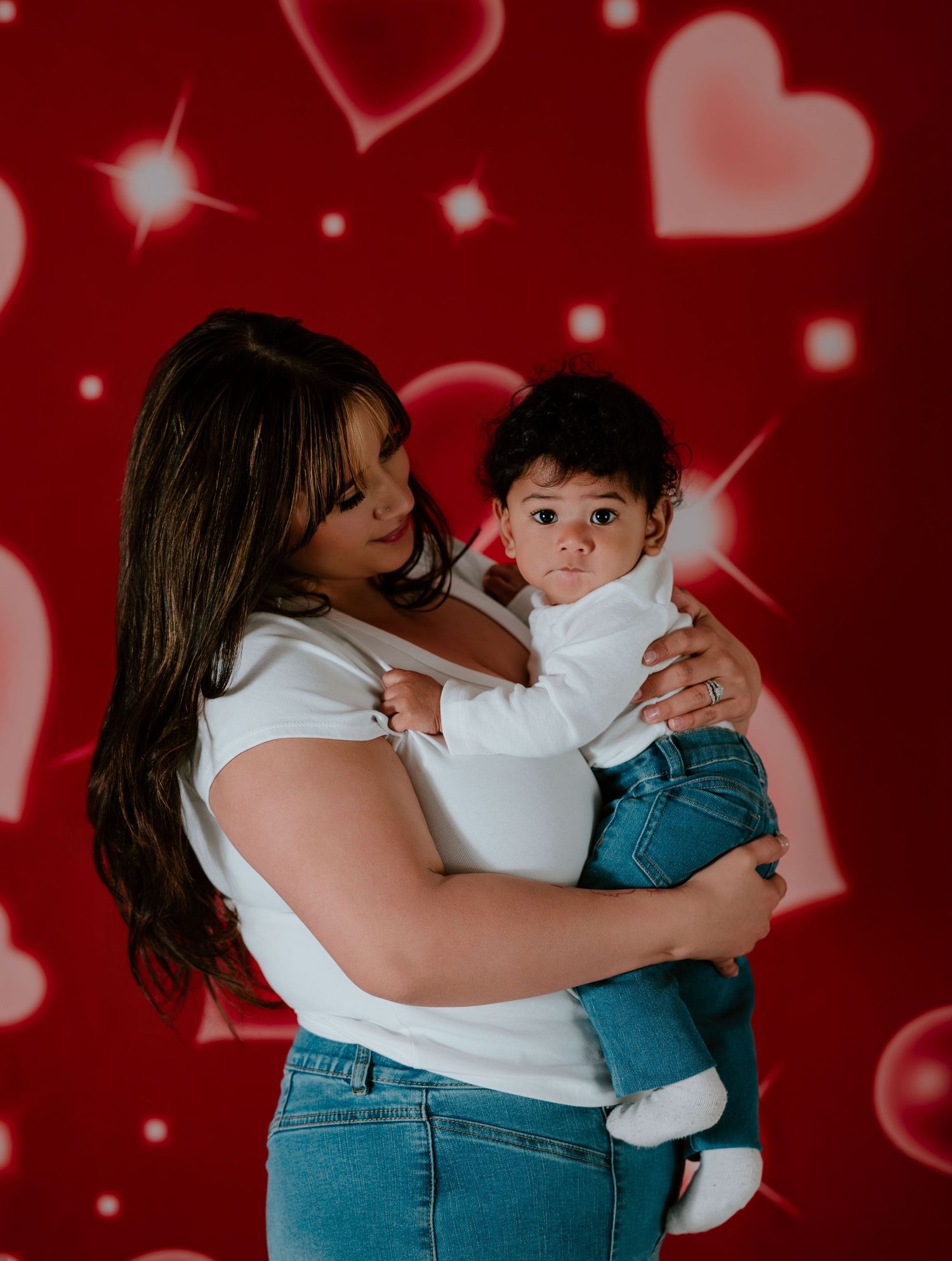 A series of four photos showing tender moments between parent and baby against a red background with floating heart shapes.