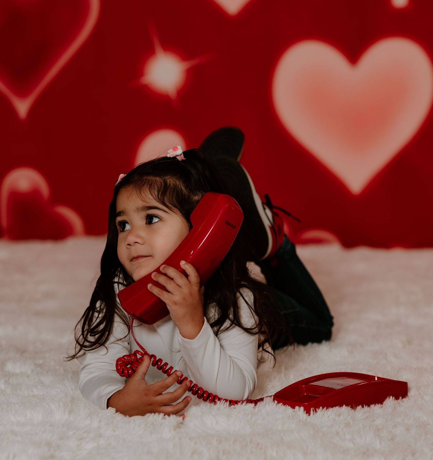 A person in red and white lying on a white surface with heart-shaped bokeh lighting in the background.