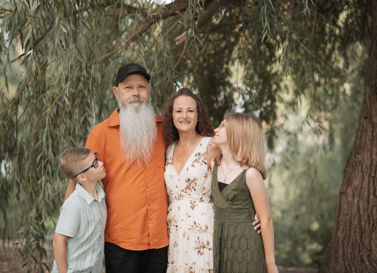 Family posed under green willow tree for a family photo session at Manito Park in Spokane Washington.