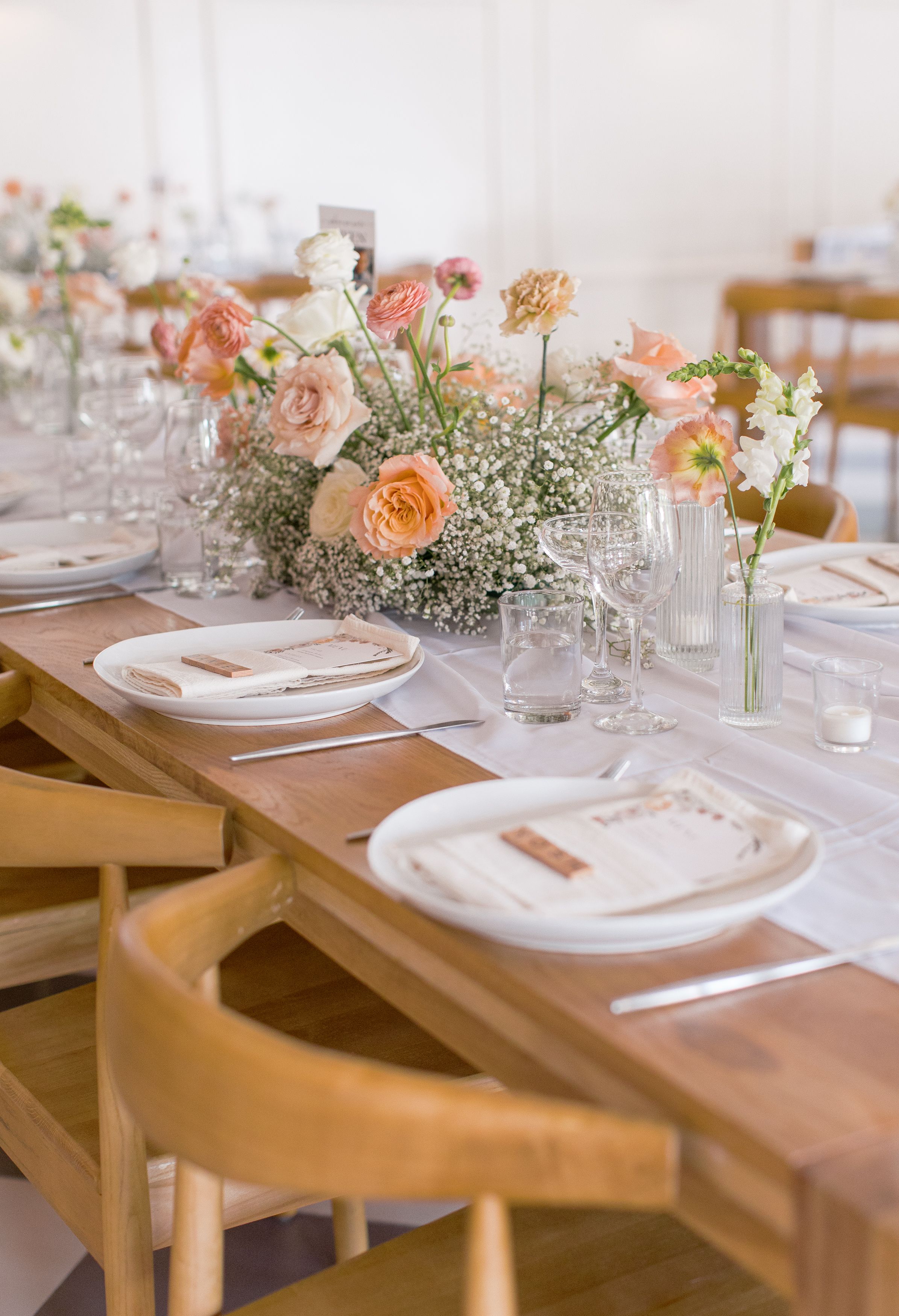 Elegant table setting with peach roses and baby's breath centerpiece on wooden table with formal place settings.