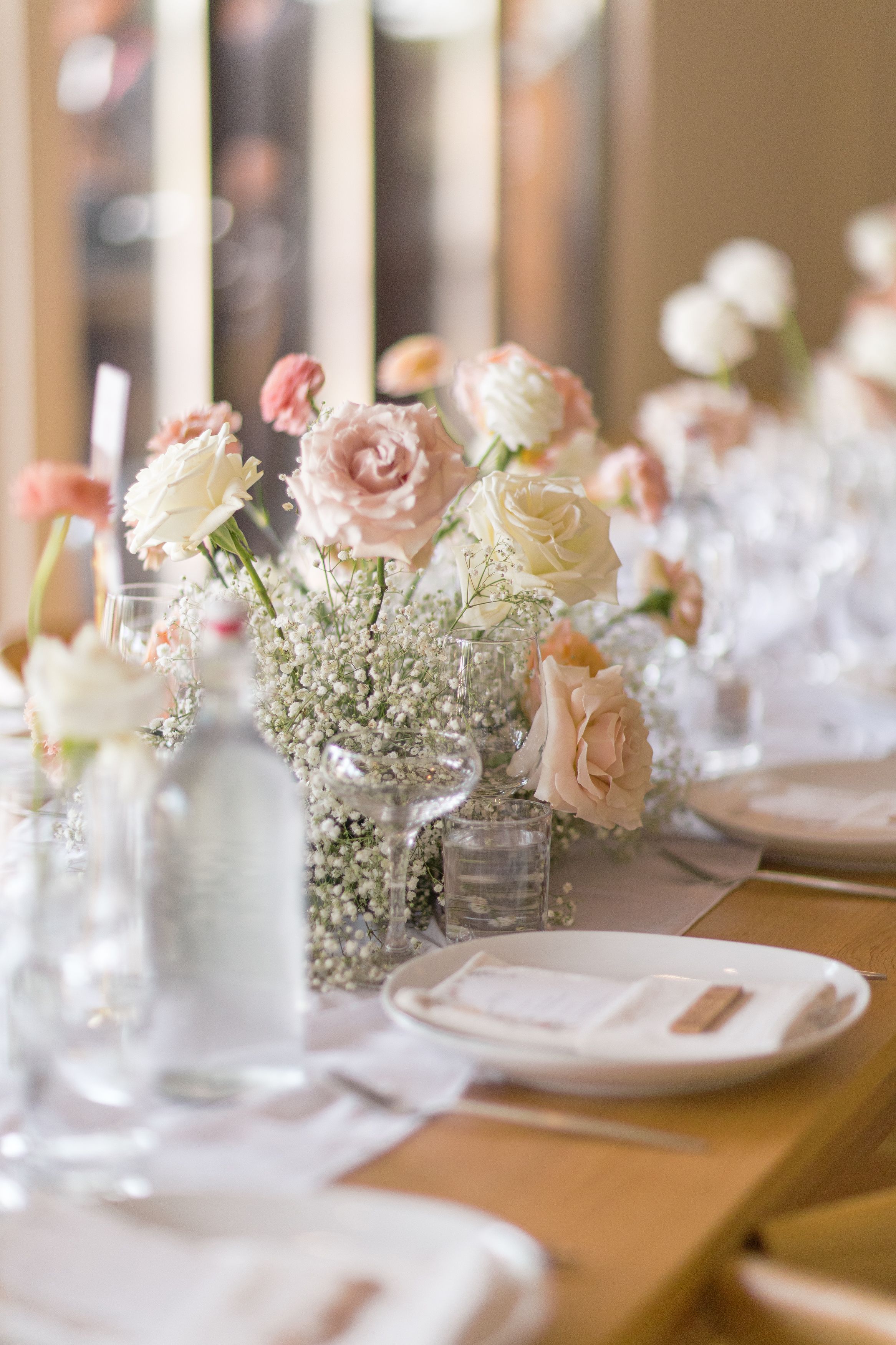 Table setting at an elegant wedding reception with pink roses, baby's breath flowers, and crystal glassware on display.