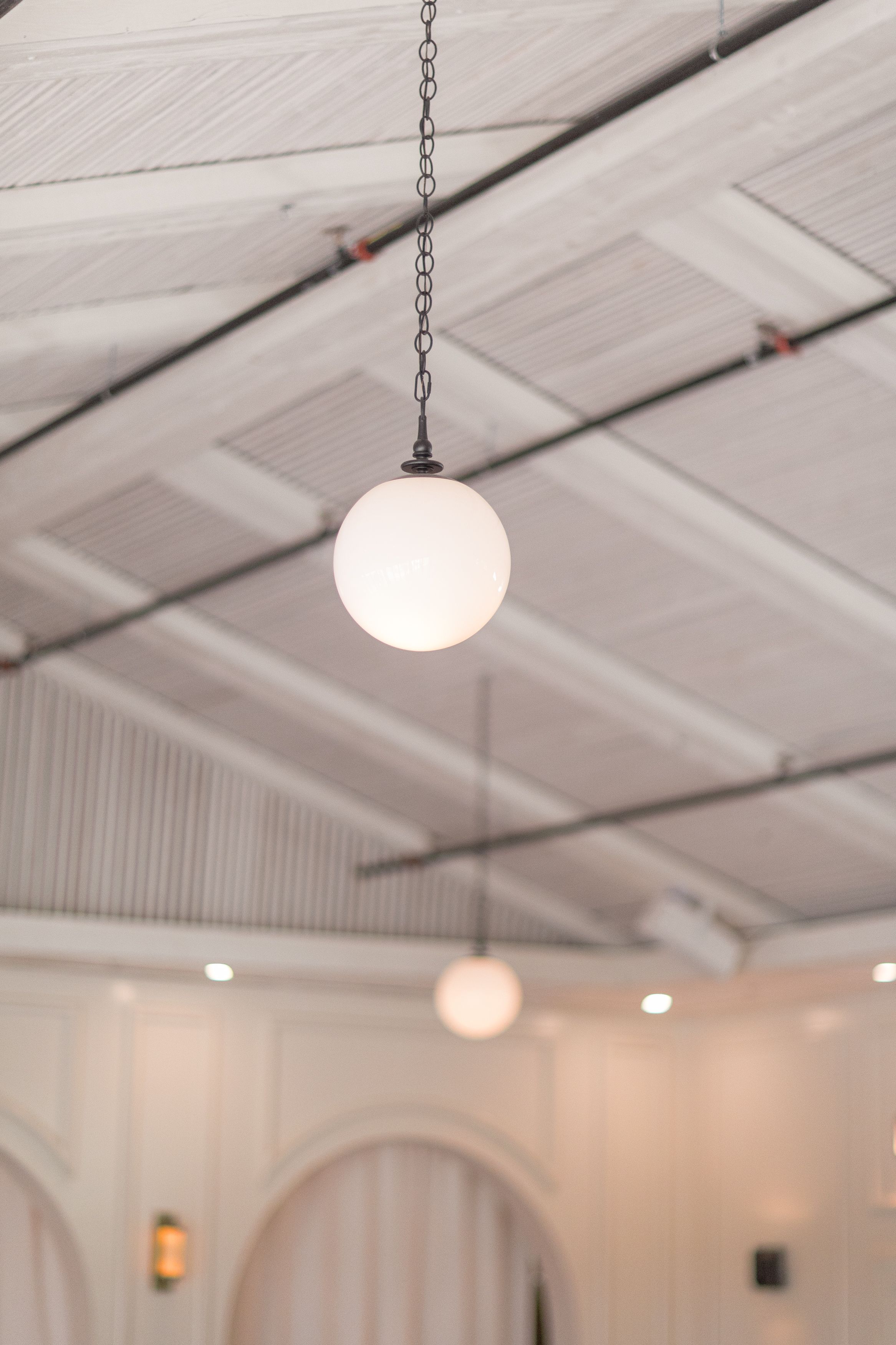 Pendant globe lights hang from white beamed ceiling with industrial style in a modern interior space.