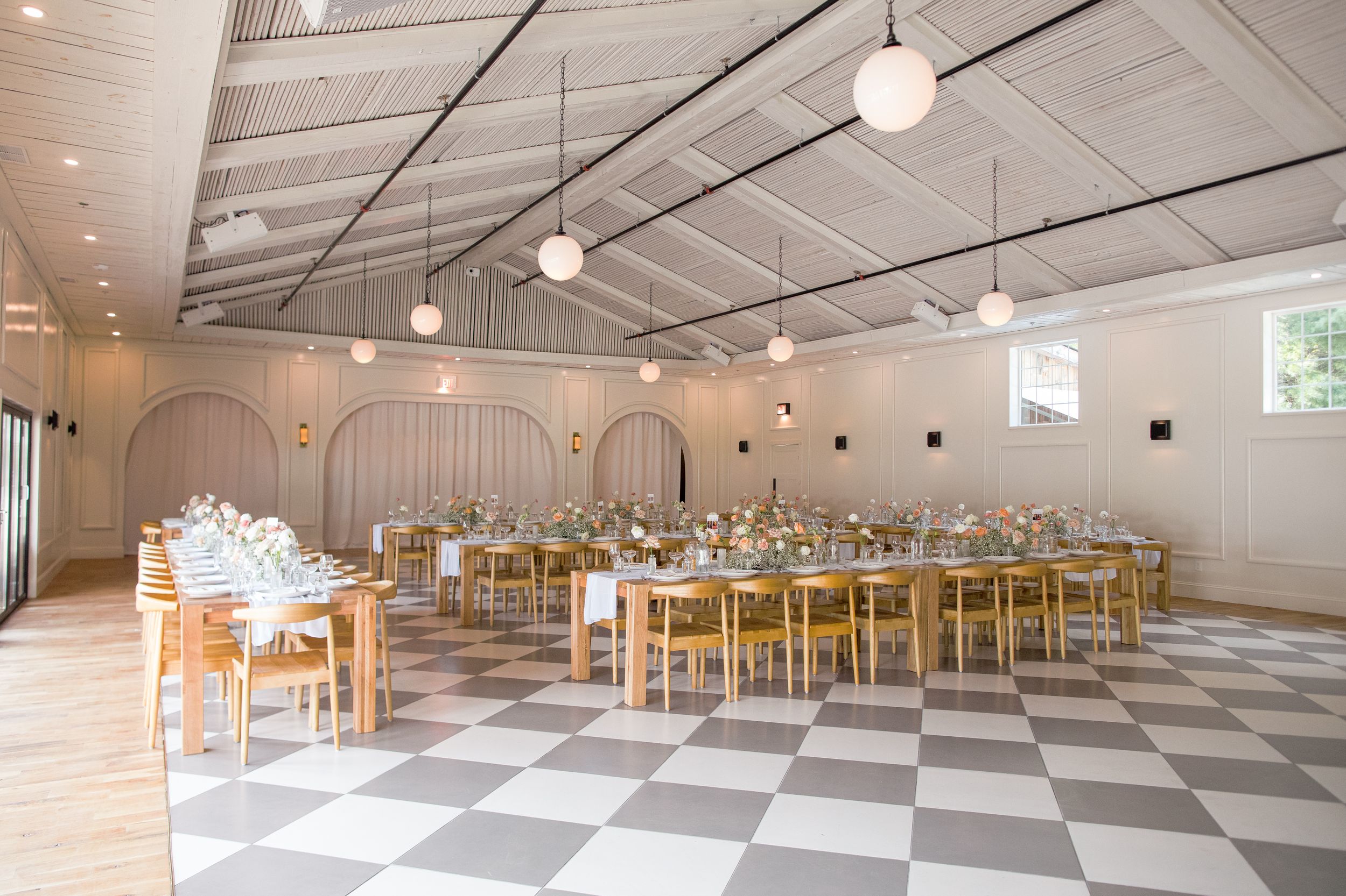 A spacious white wedding reception venue with checkered floors and golden chairs set up in elegant rows.