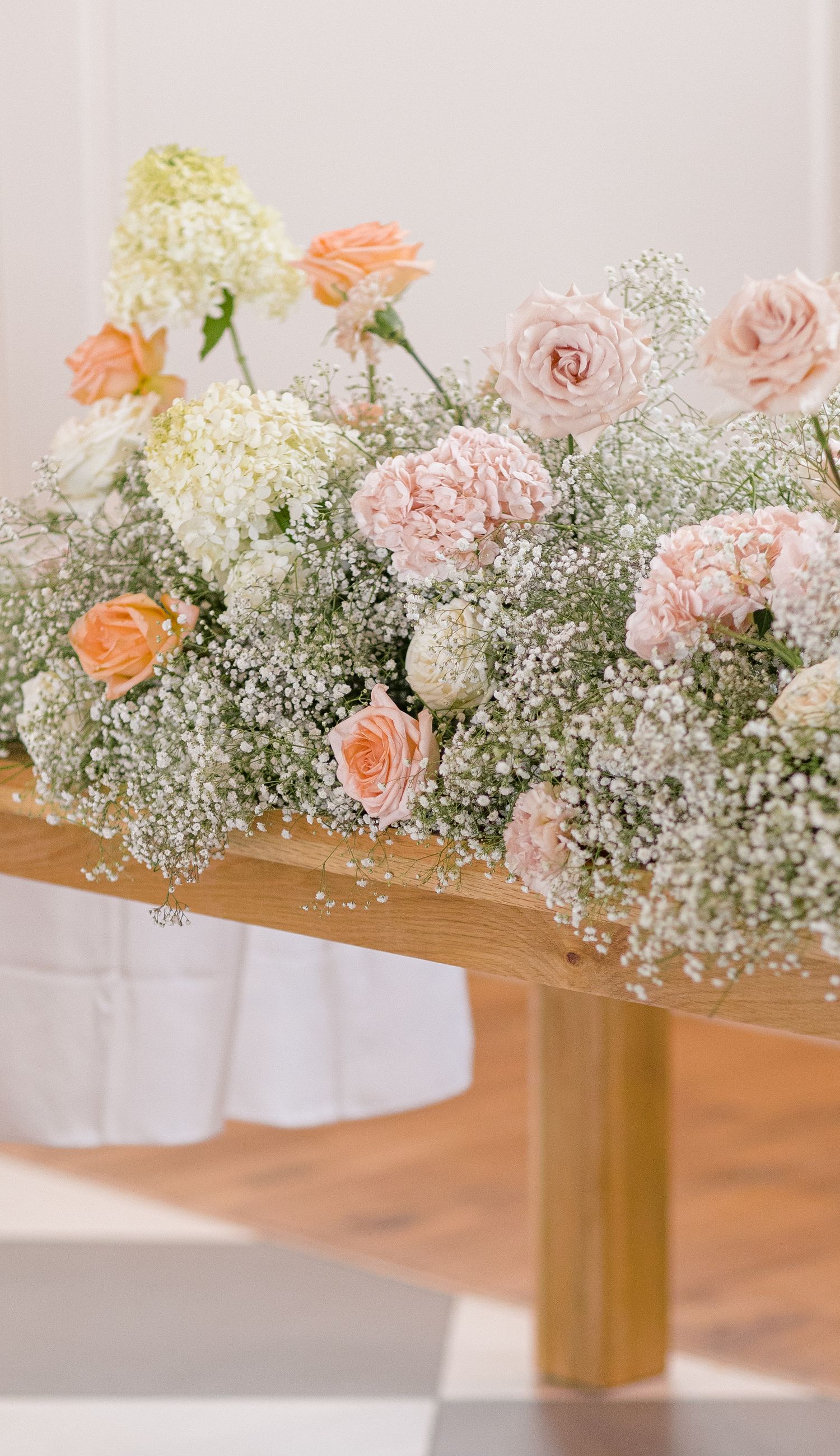 Elegant floral centerpiece featuring pink roses, peach carnations, and delicate baby's breath on a wooden surface.
