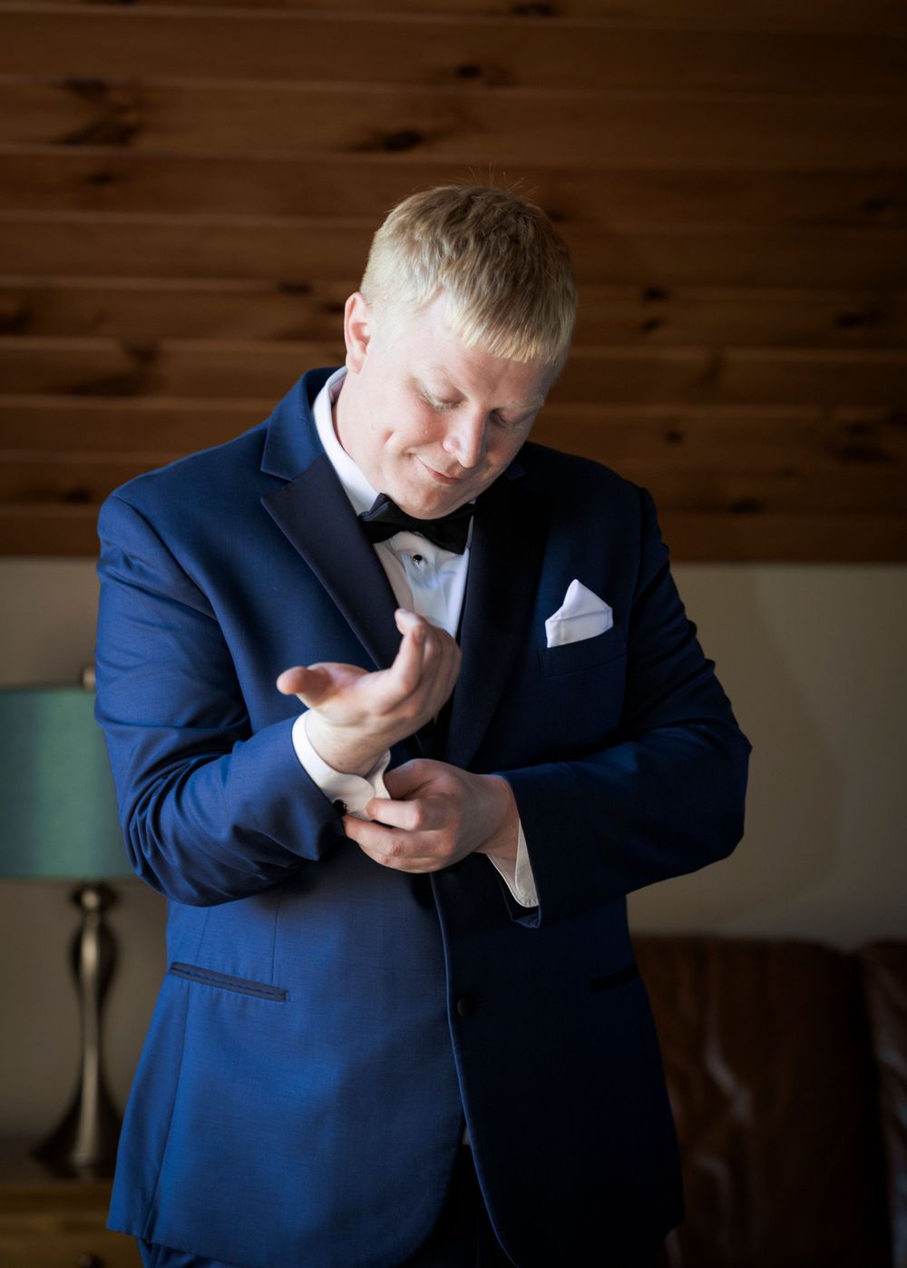 Groom in navy suit adjusts his tie while getting ready.
